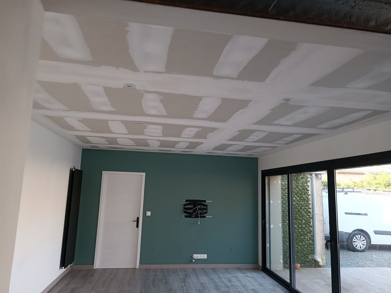 Plafond en plaques de plâtre bandé avec spots encastrés, mur vert et baie vitrée